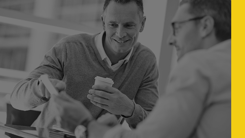 man drinking coffee and looking at document with his friend