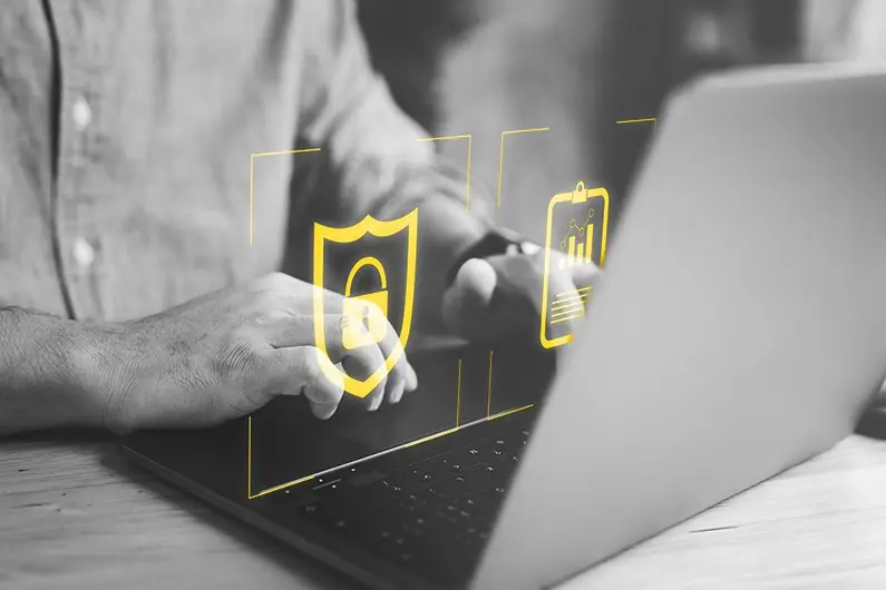 Icon of shield with lock and charts in yellow over black and white photo of man's hands typing on laptop