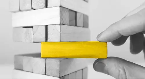 Fingers pulling a yellow puzzle piece out of a tower