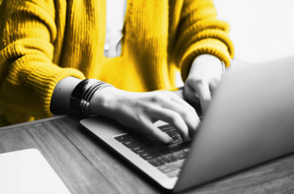 Person's torso in a yellow sweater, hands typing on a laptop