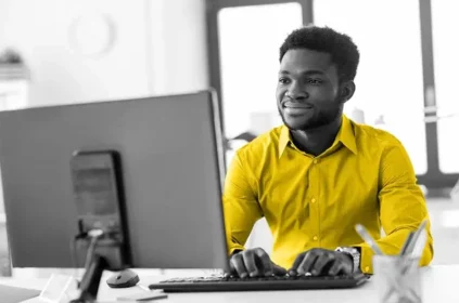 A man in a yellow shirt typing on a computer