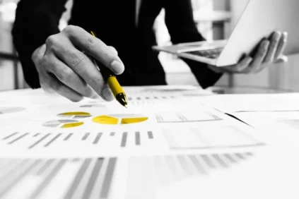 A man holding a yellow pen over yellow charts and graphs