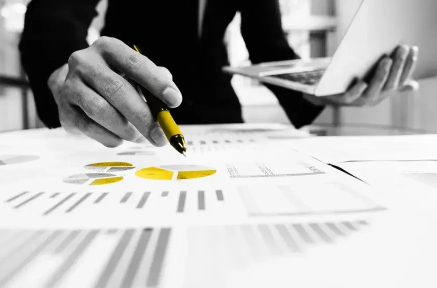 A man holding a yellow pen over yellow charts and graphs